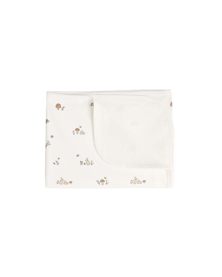 A folded white "swaddle in bunnies" by quincy mae, featuring small brown and beige animal and mushroom prints, displayed on a plain white background.