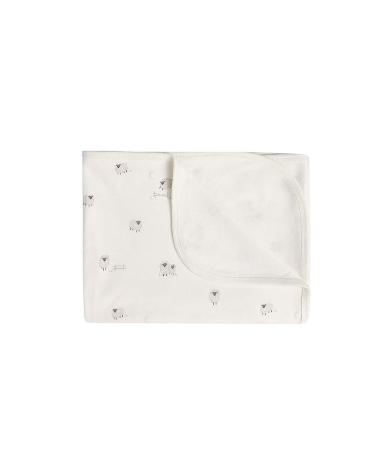 A folded white Quincy Mae swaddle in sheep, featuring small gray animal and heart patterns, is displayed on a white background. One corner of the soft organic cotton blanket is turned up to reveal its gentle texture—perfect for wrapping your baby.