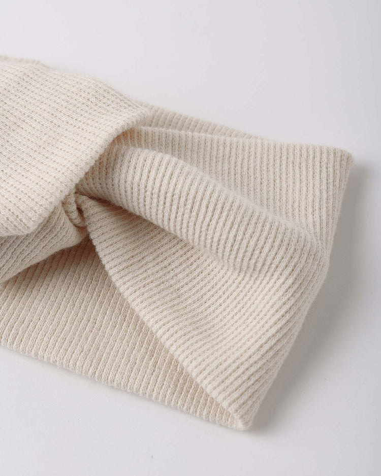 Close-up of the quincy mae knotted headband in ecru, a cream-colored, ribbed organic cotton accessory with a twisted knot design for baby girls, shown laid flat on a white surface.