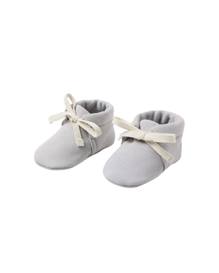 A pair of quincy mae baby booties in cloud, crafted from soft organic cotton in light gray with white fabric laces, are placed side by side on a white background.