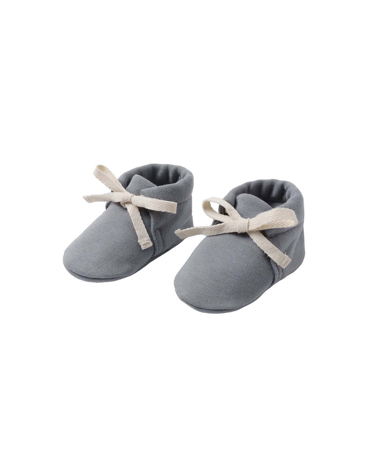 A pair of quincy mae baby booties in slate, crafted from organic cotton and featuring cream-hued fabric laces, are placed side by side on a white background.