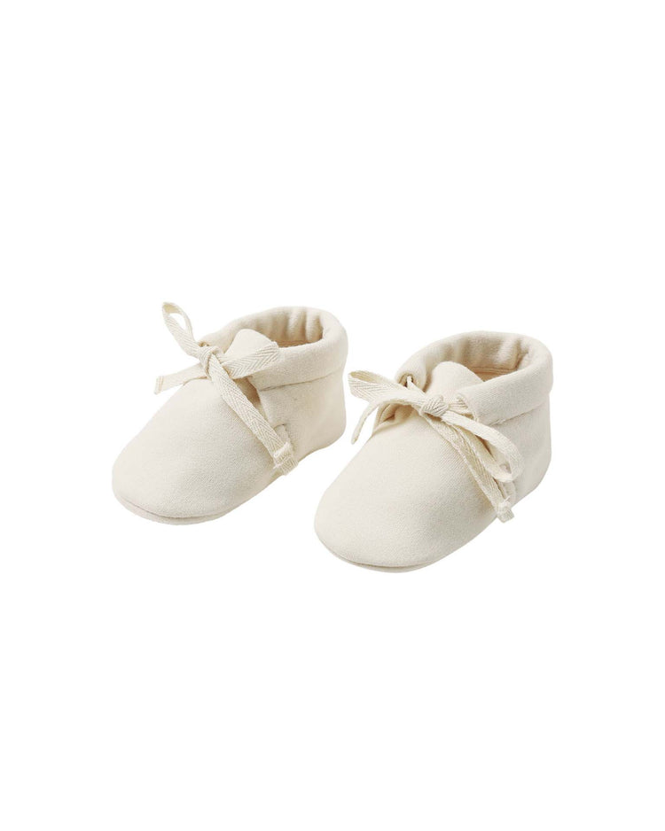 A pair of “baby booties in natural” by Quincy Mae, crafted from organic cotton with delicate fabric laces and shown on a plain white background.