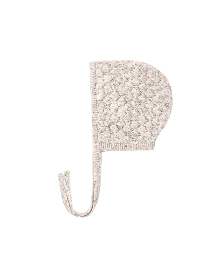 The knit bonnet in natural confetti by quincy mae is crafted from soft organic cotton with a textured, bubble-like pattern and two long, flat ties. This cozy baby bonnet is shown on a plain white background.