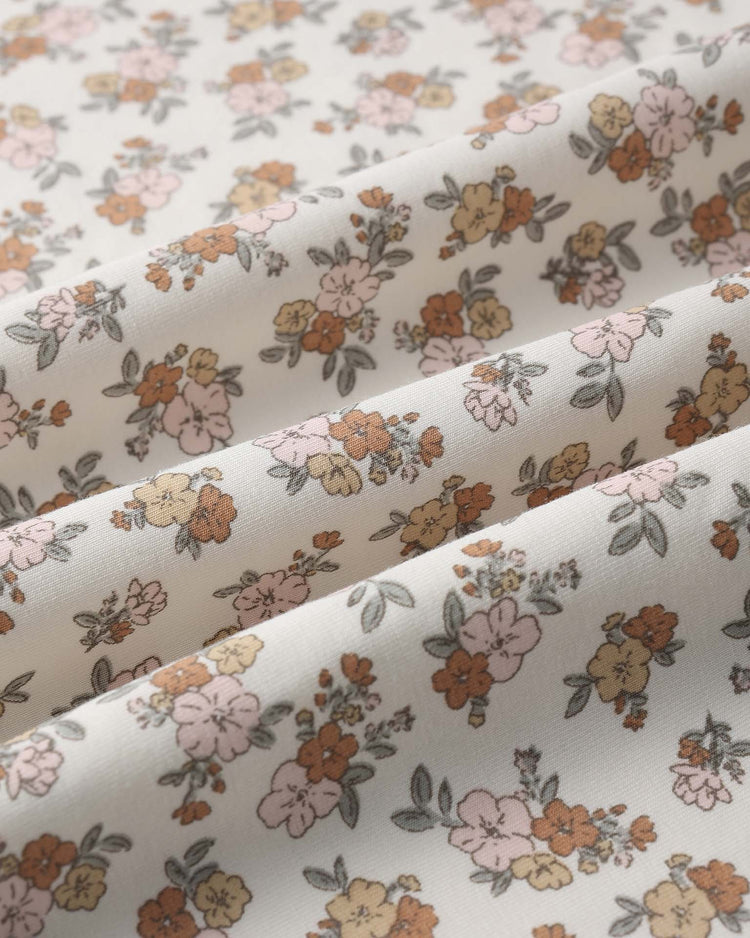 Close-up of the quincy mae bamboo swaddle in wildflower, featuring cream-colored fabric with a vintage floral print in pink, yellow, and orange tones plus green leaves. Soft pleats highlight its gentle feel—ideal for wrapping your baby in comfort.