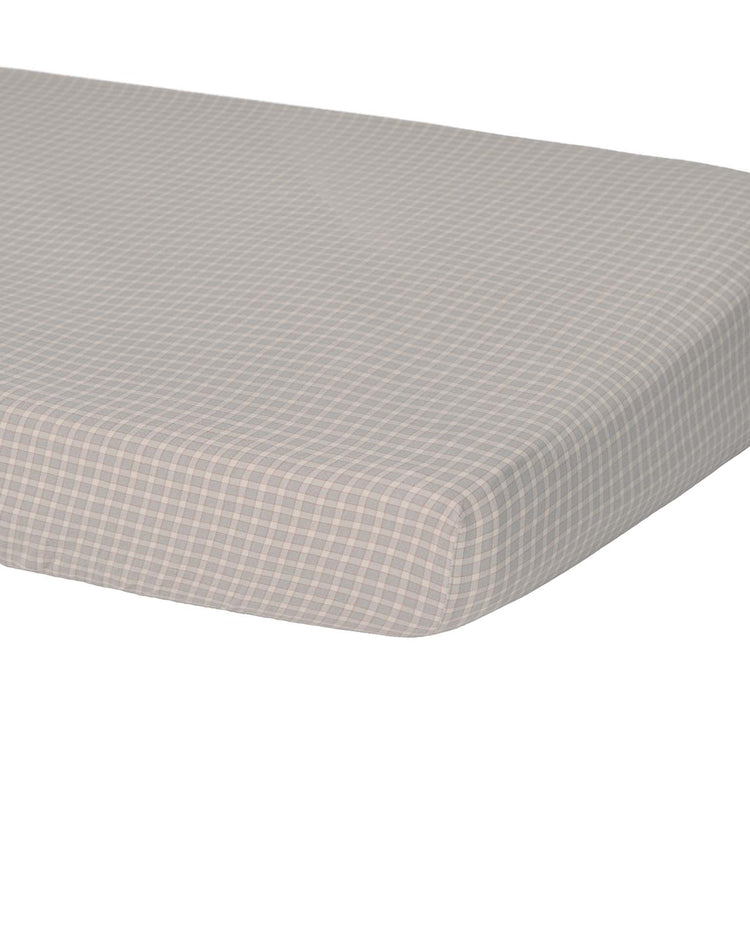 A close-up of a rectangular mattress or cushion fitted with the quincy mae woven crib sheet in blue gingham, featuring a small, light blue and white checkered pattern against a white background.