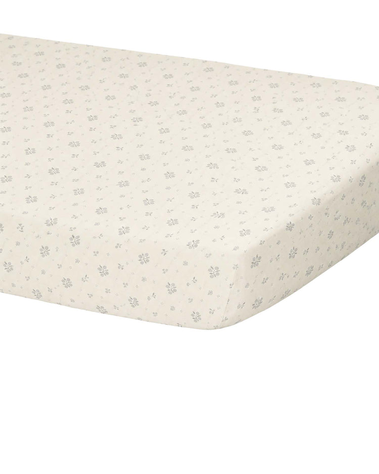 A close-up of the Quincy Mae woven crib sheet in winter berry, featuring an organic cotton fabric with a cream background and a delicate gray floral print, snugly fitted around the corner of a crib mattress.