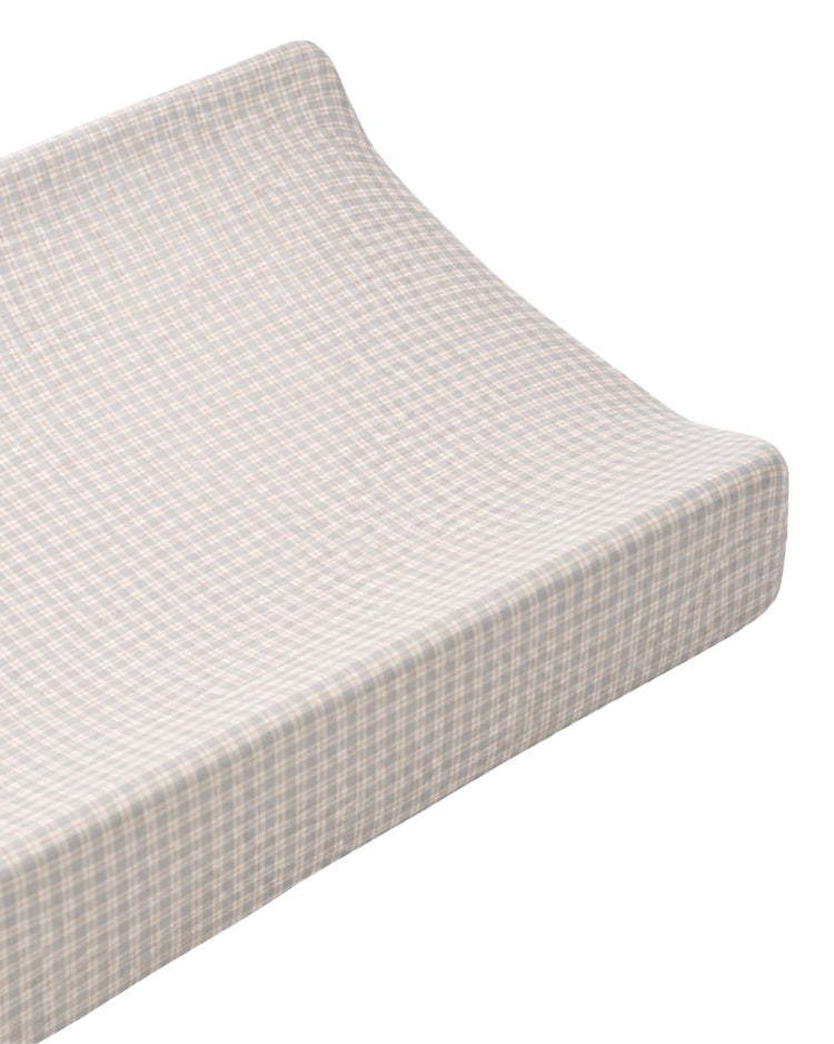 A quincy mae changing pad cover in blue gingham, shown at an angle on a white background, adds comfort to a contoured changing pad with its soft organic cotton fabric.