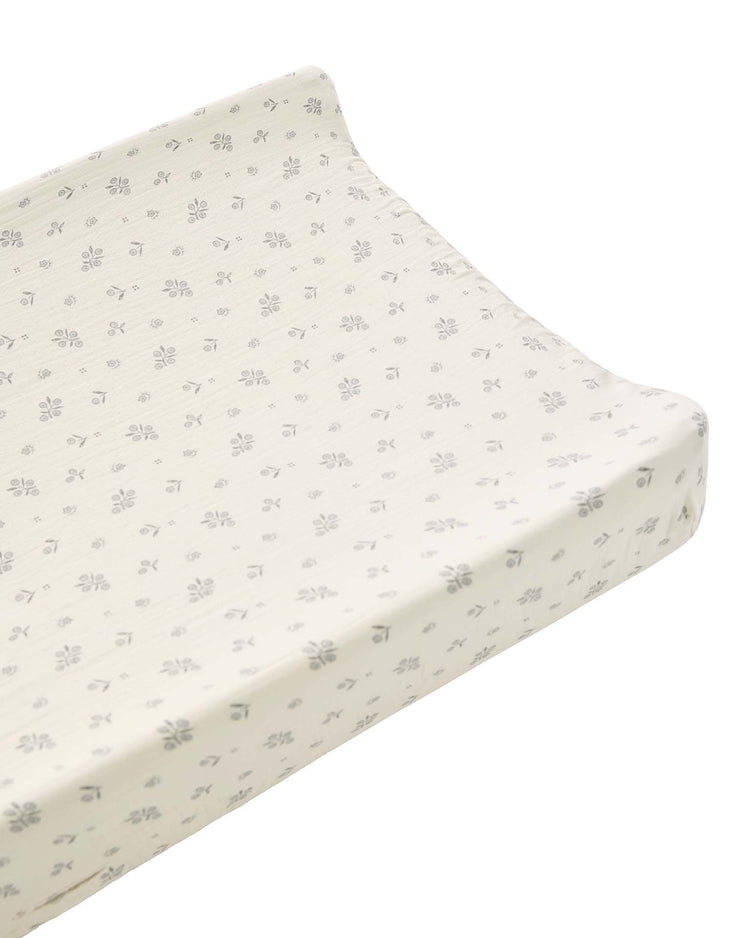 A contoured changing pad is covered with the quincy mae changing pad cover in winter berry, crafted from organic cotton in a cream-colored fabric featuring a small gray floral pattern, and is shown on a plain white background.