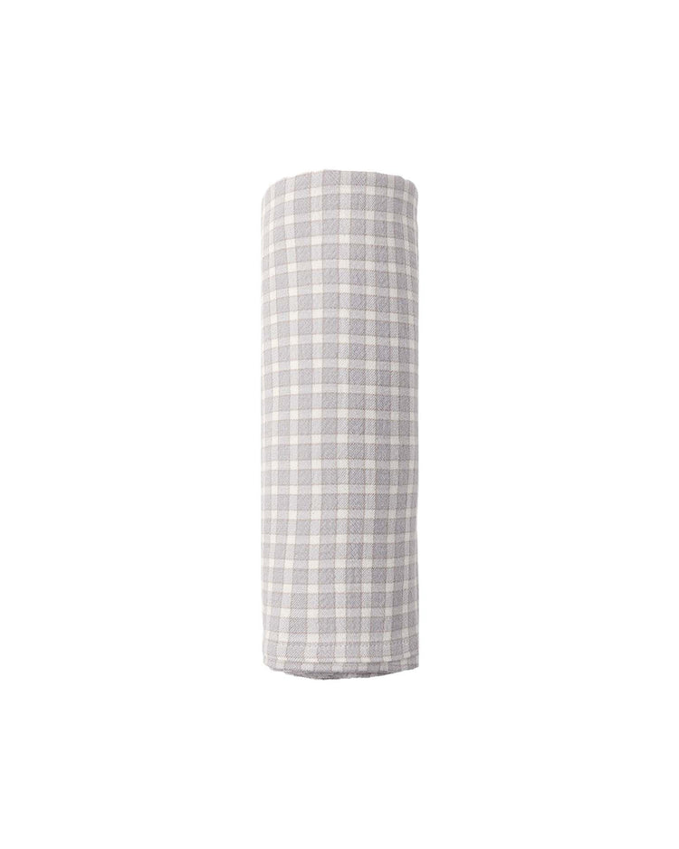 A woven swaddle in blue gingham by quincy mae, reminiscent of a breathable baby blanket, is displayed rolled up and upright against a plain white background.