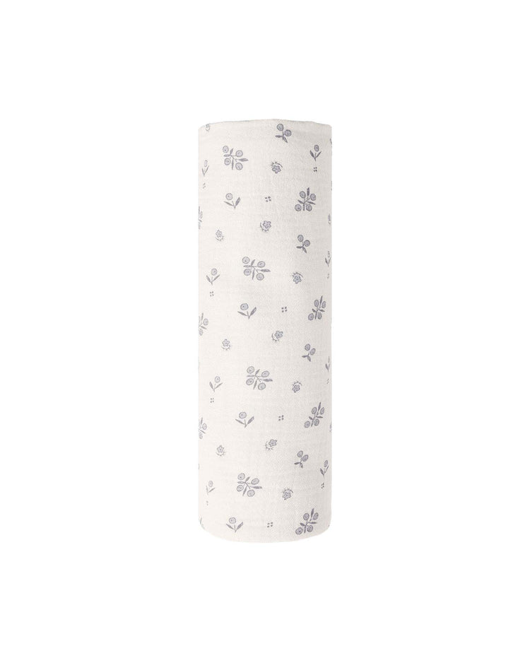 The quincy mae woven swaddle in winter berry, featuring a soft off-white organic cotton fabric adorned with a delicate blue floral and leaf design, is shown standing upright against a simple white background.