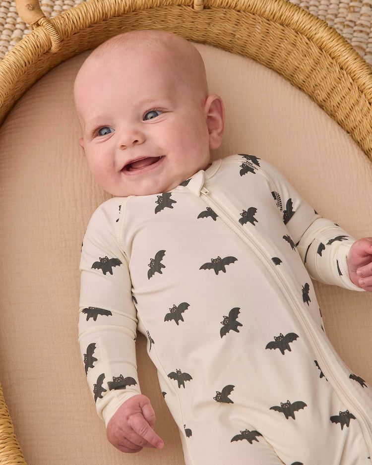 A smiling baby lies in a woven bassinet, wearing the quincy mae bamboo zip footie in bats.