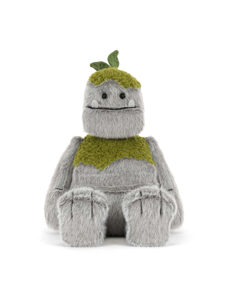 The Jellycat Rockleton is a gray plush toy with green moss-like patches, small horns, and round black eyes. Made of polyester, this stuffed animal sits upright against a white background.