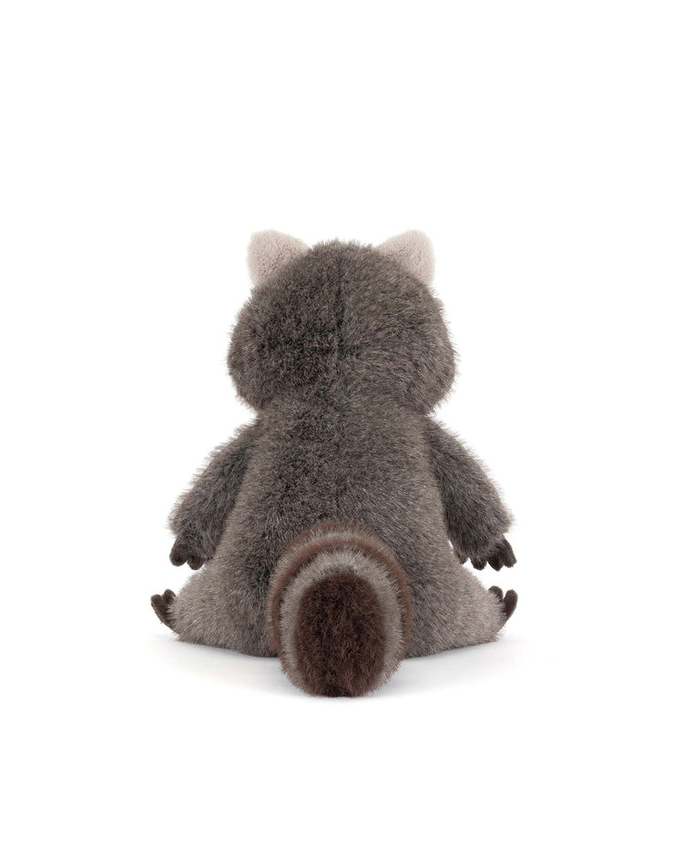 The jellycat trixiwoo raccoon plush toy sits with its back to the viewer, showing off soft gray fur, a striped tail, and small ears on a white background.