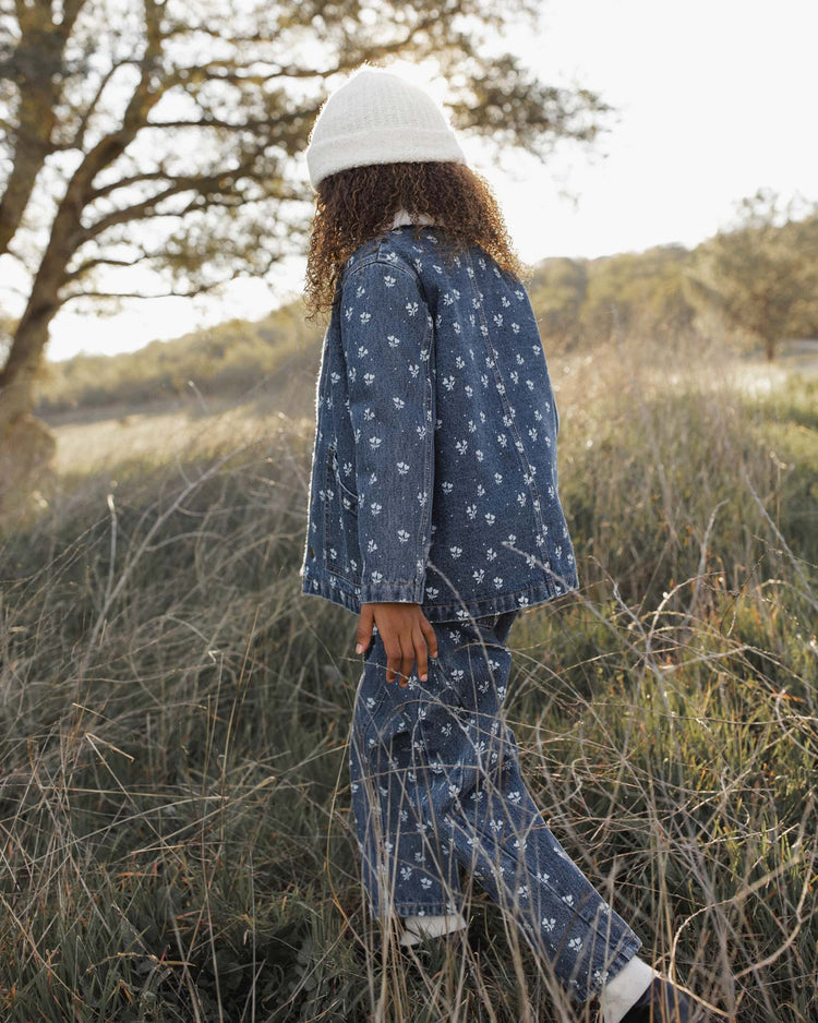 A child with curly hair, wearing a white beanie and the rylee + cru long chore coat in heart ditsy with shearling lining, walks through tall grass in a field with trees in the background.