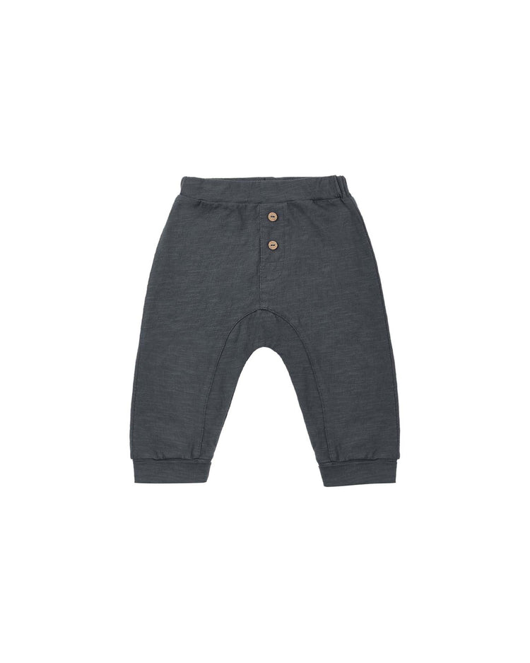 PREORDER rylee + cru baby cru pant in midnight, made from 100% cotton, features a dark gray color, an elastic waistband with two brown buttons on the front, cuffed ankles, and is displayed on a white background.