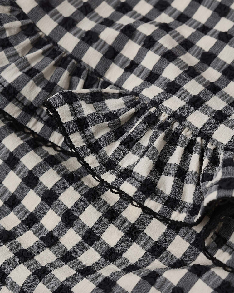 Close-up of the rylee + cru skirted one-piece in black gingham, featuring ruffled details, a textured dot pattern, and UPF 50+ protection for stylish sun safety.