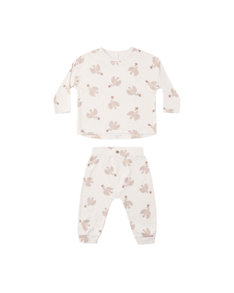 The rylee + cru long sleeve tee + pant set in sparrows is a two-piece children’s pajama set crafted from soft cotton jersey, featuring a white background with a delicate light brown sparrow pattern. Designed for comfort and convenience, the top includes shoulder snaps for easy dressing. The pajamas are laid flat on a plain white surface.