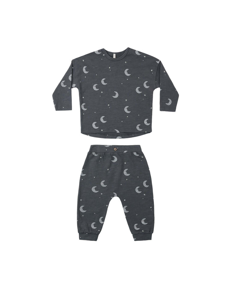 The rylee + cru PREORDER long sleeve tee + pant set in moons is a children’s two-piece pajama set, crafted from soft cotton jersey in dark gray and featuring an all-over white moons and stars print. The set is laid flat on a white background.