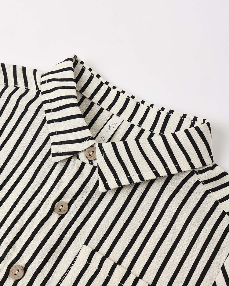 A close-up of the rylee + cru collared short sleeve shirt in wavy stripe, featuring a cream color, vertical black stripes, brown buttons, and a visible clothing tag near the collar, displayed flat on a white surface.
