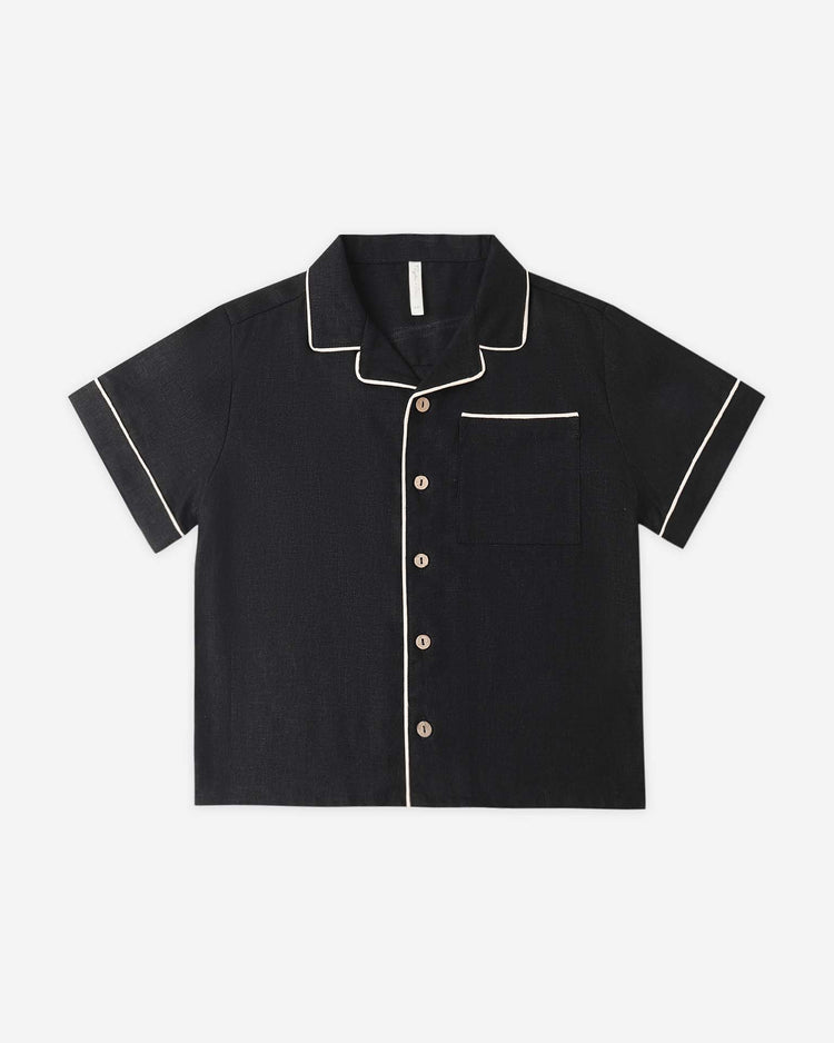 The rylee + cru lapel collared shirt in black for boys features short sleeves and white piping on the collar, sleeves, pocket, and front; displayed flat on a white background.