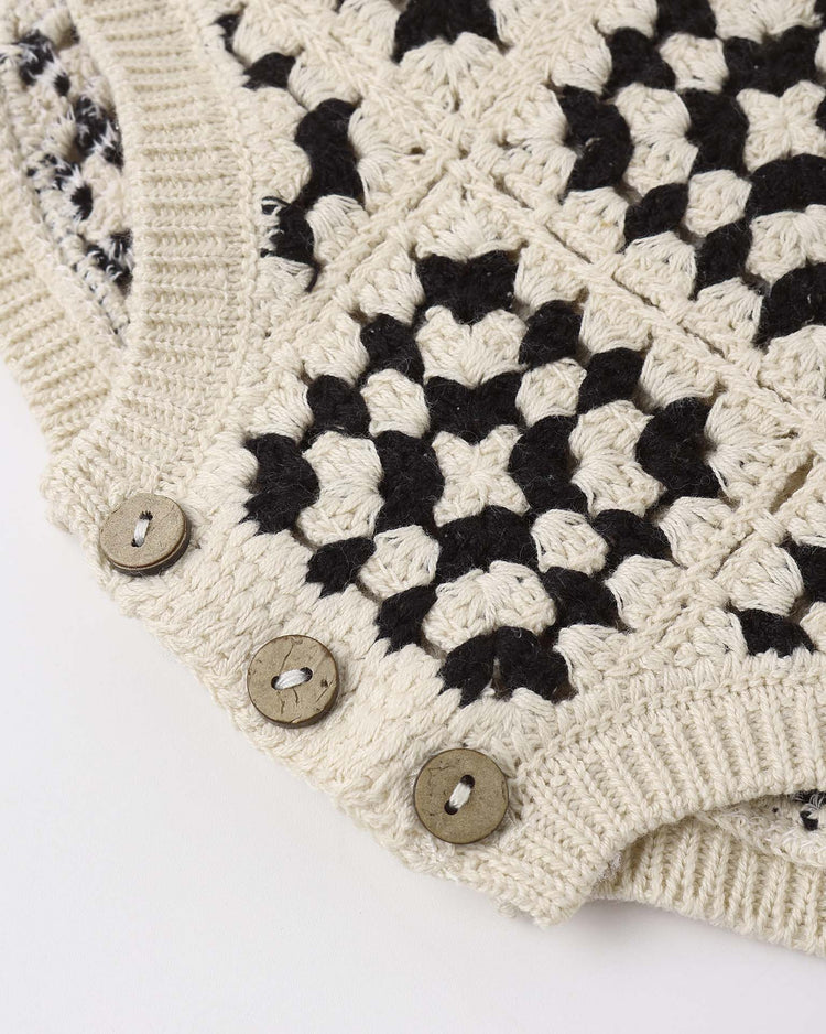 Close-up of the rylee + cru crochet romper in abstract, made from 100% cotton with a black and cream geometric knit, ribbed edge, and three round beige buttons. Detailed stitching gives it a subtle vintage charm.