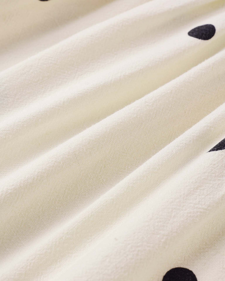 Close-up of the cream-colored "harper dress in polka dot" by rylee + cru, featuring soft linen-viscose folds and scattered black polka dots—a stylish choice for a coordinating bloomers set or babydoll tank dress.