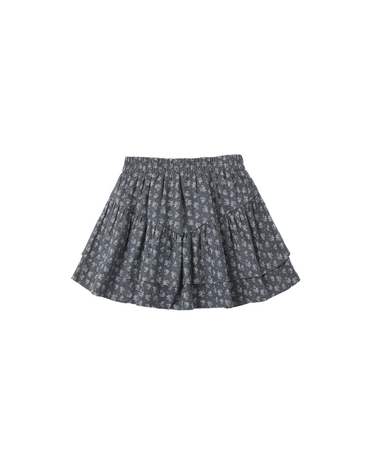 The rylee + cru tiered mini skirt in heart ditsy is a short, dark gray skirt with an elastic waistband, small white heart print, and a ruffled, tiered design.