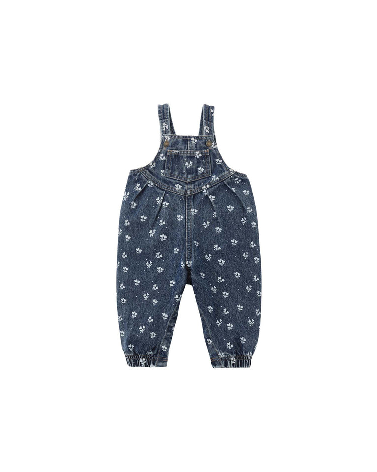 The “vintage overall in heart ditsy” by rylee + cru features a charming white floral pattern printed throughout on blue denim, designed for children with adjustable shoulder straps, button closures, and elasticized cuffs at the ankles for a comfortable fit. Made from 100% cotton.