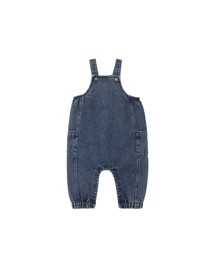 The rylee + cru cargo baby overall in indigo, crafted from 100% cotton with adjustable shoulder straps, front buttons, side pockets, and elasticized ankles, is shown against a white background.