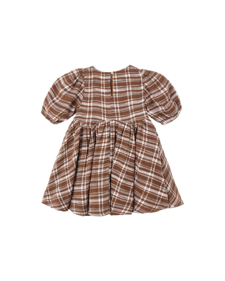 The “rose dress in aspen plaid” by rylee + cru features a brown and white check pattern, short puff sleeves, and a gathered skirt, shown laid flat on a white background. The back is detailed with two small buttons at the neckline.