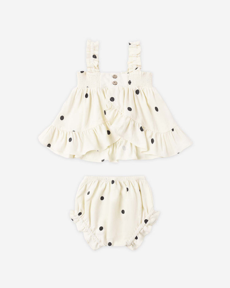 The lala set in polka dot by rylee + cru is a baby girls’ two-piece outfit with a sleeveless white top featuring black polka dots and ruffle details, plus matching flutter bloomers.
