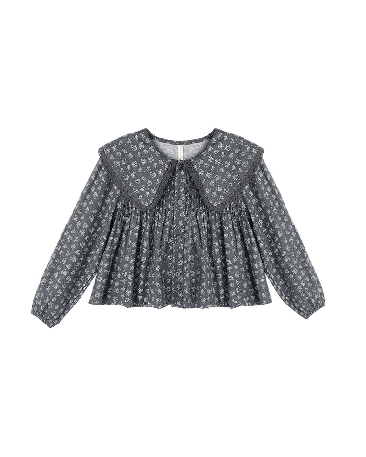 The “fern blouse in heart ditsy” by rylee + cru is a gray long-sleeved top featuring a wide, rounded crochet lace-trim collar and an all-over small white heart ditsy print. Pleats below the collar and front buttons add charming details.