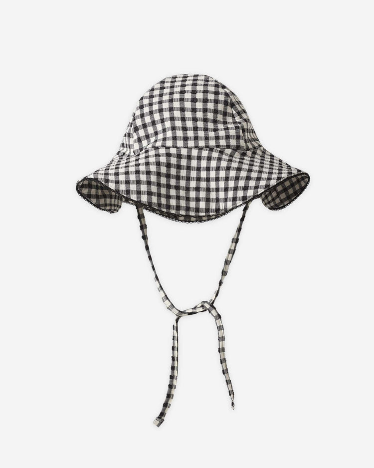 The rylee + cru swim hat in black gingham features a wide brim and matching checkered chin straps tied in a bow, made from recycled polyester with UPF 50+ protection, shown on a white background.