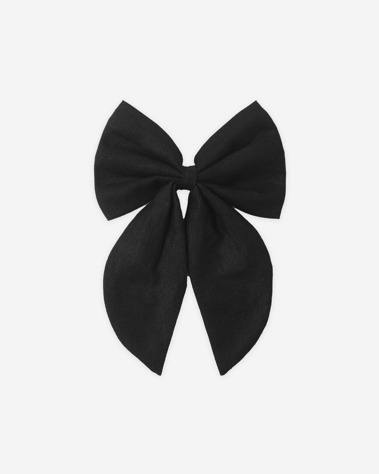 The oversized bow in black by rylee + cru features a large black linen design with two loops and long tails, displayed on a plain white background.