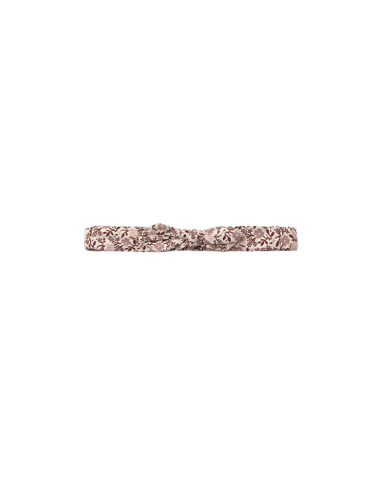 A baby bow headband in primrose by rylee + cru, featuring a thin, light pink band with a delicate dark brown floral pattern and a small central knot, crafted from 100% cotton for an ultra-soft feel.