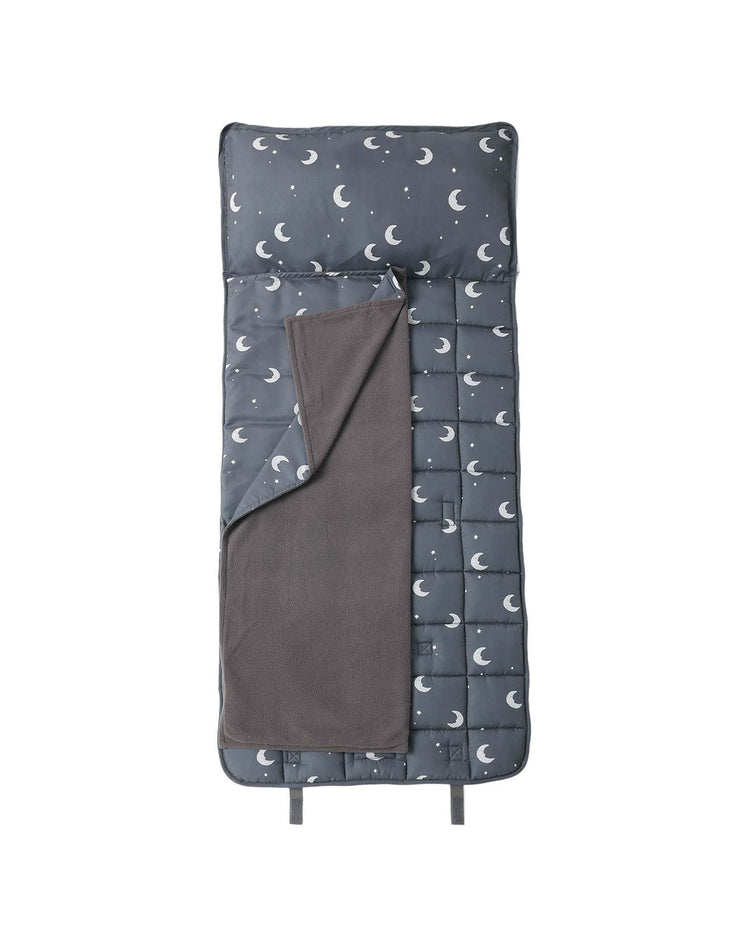 A “nap mat in moons” by rylee + cru, shown on a white background, features a dark gray color with a charming moon and star pattern, includes a removable pillow for convenience, and comes with a soft micro-fleece blanket that is partially folded back.
