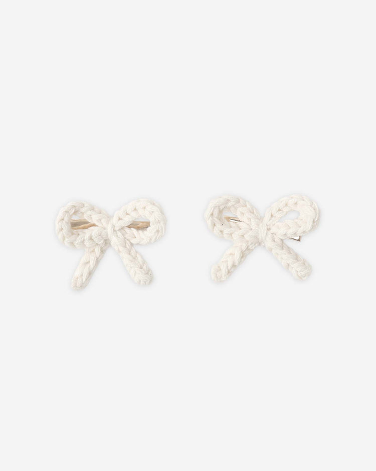 Two rylee + cru crochet bow clips in ivory, made from soft cotton and shaped into delicate bows, are displayed side by side on a plain light background.