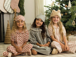 Three children in pajama sets sitting in front of a Christmas tree.