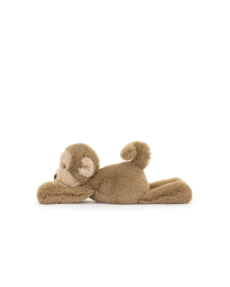 The smudge monkey tiny by Jellycat is a fun, chunky toy with brown plush fur, lying on its stomach with arms extended forward, making it the perfect fluffy friend.