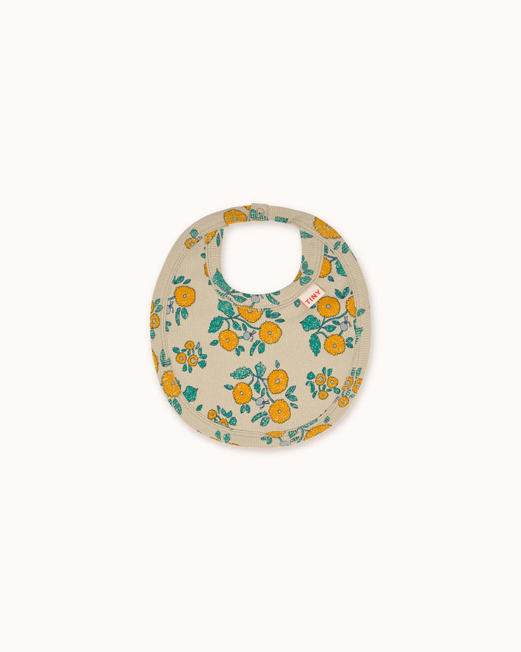 A dark vanilla baby bib adorned with a distinctive print of yellow and blue flowers, capturing the signature style of tiny cottons.