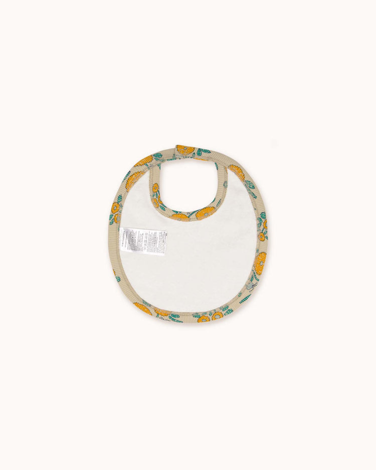 The flowers bib in dark vanilla by tiny cottons features a white center and beige border with unique prints of colorful cars and vehicles, showcasing high-quality craftsmanship.
