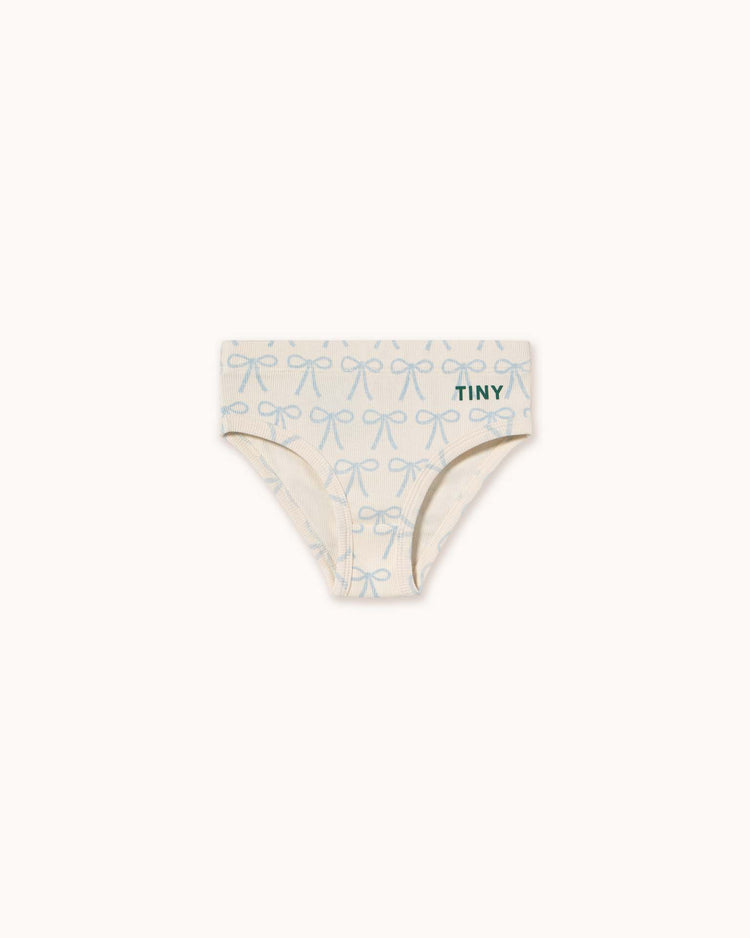 The "bows briefs in off-white" by tiny cottons feature a light cream background with blue bows and have "TINY" printed on the waistband, exemplifying the brand's high-quality clothing.