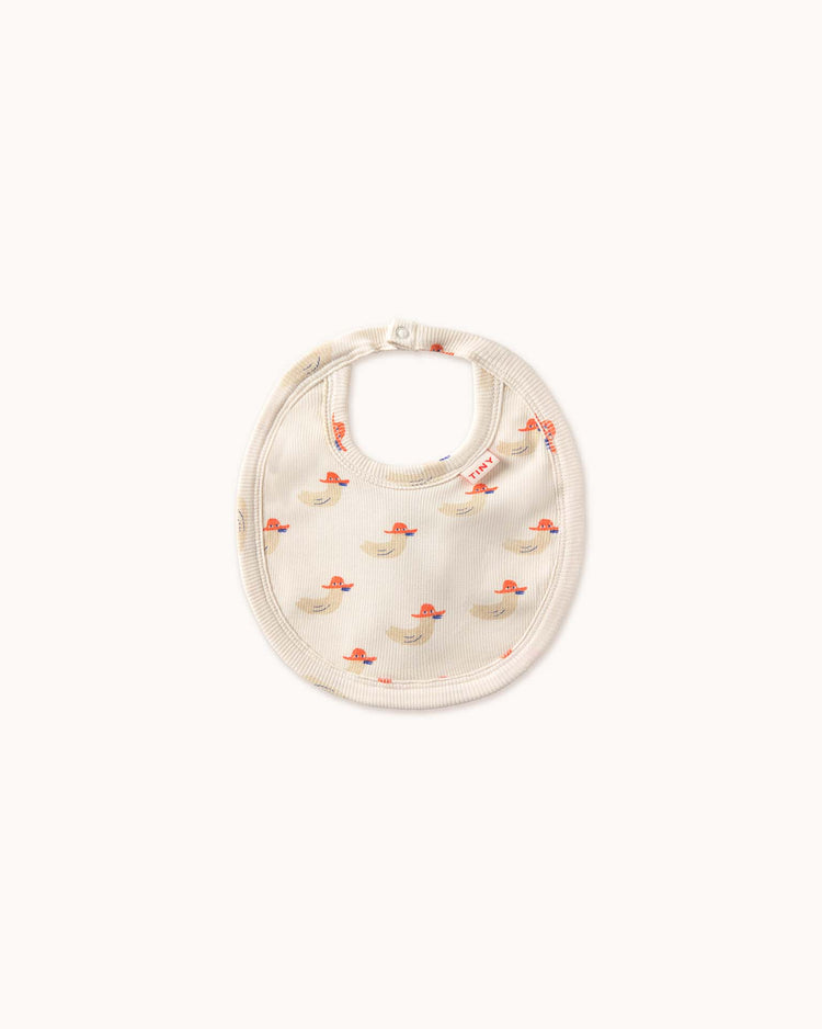 The off-white baby bib from tiny cottons, featuring a charming duck pattern and a secure snap closure, showcases the brand's dedication to high-quality clothing.