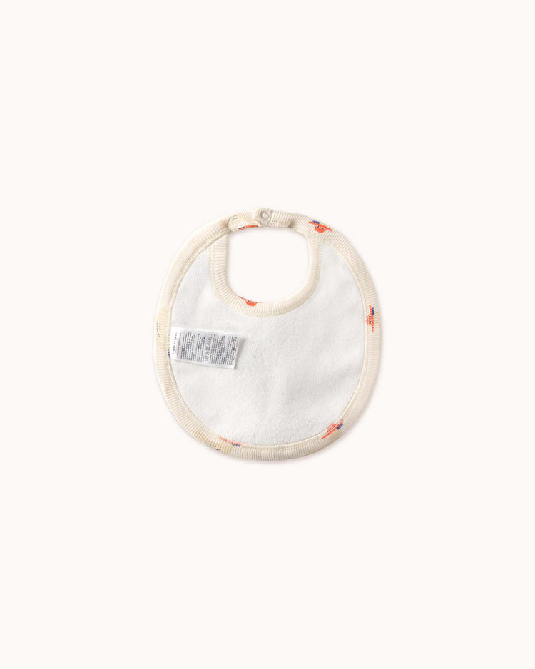 The ducks bib in off-white by tiny cottons is an organic cotton baby bib with a small print design and care label on a plain background, ideal for those who value high-quality clothing for their infants.