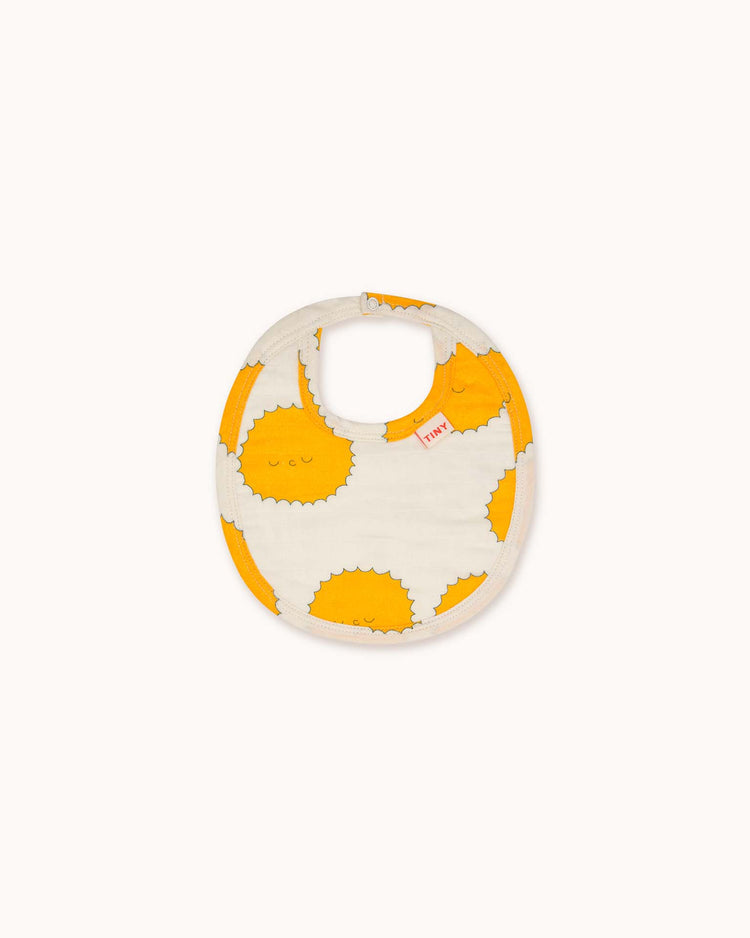 The Tiny Cottons sun bib in off-white features a round design for children, crafted from soft organic cotton with an orange and white sun pattern, offering comfort and style for fans with its unique prints.