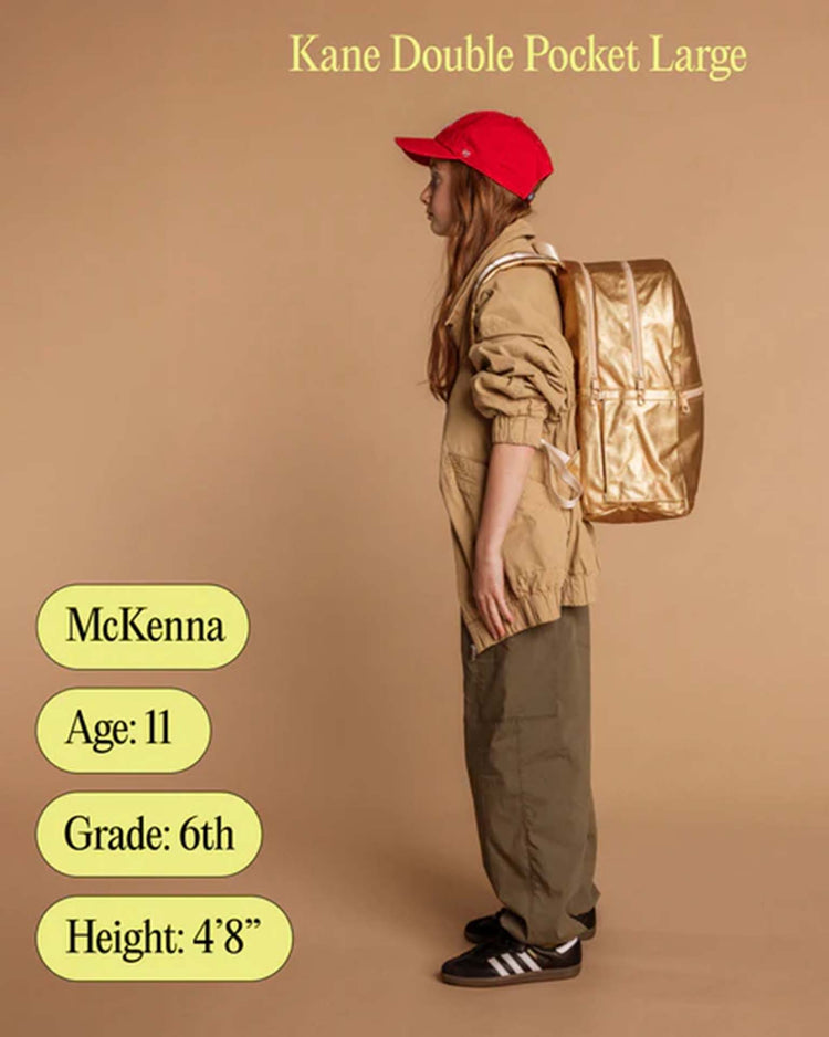 A girl in a red cap, tan jacket, green pants, and black sandals stands sideways with a Kane Large Double Pocket Backpack in Olive by STATE Bags. Text reads: McKenna, Age: 11, Grade: 6th, Height: 48. Background is a solid tan color.