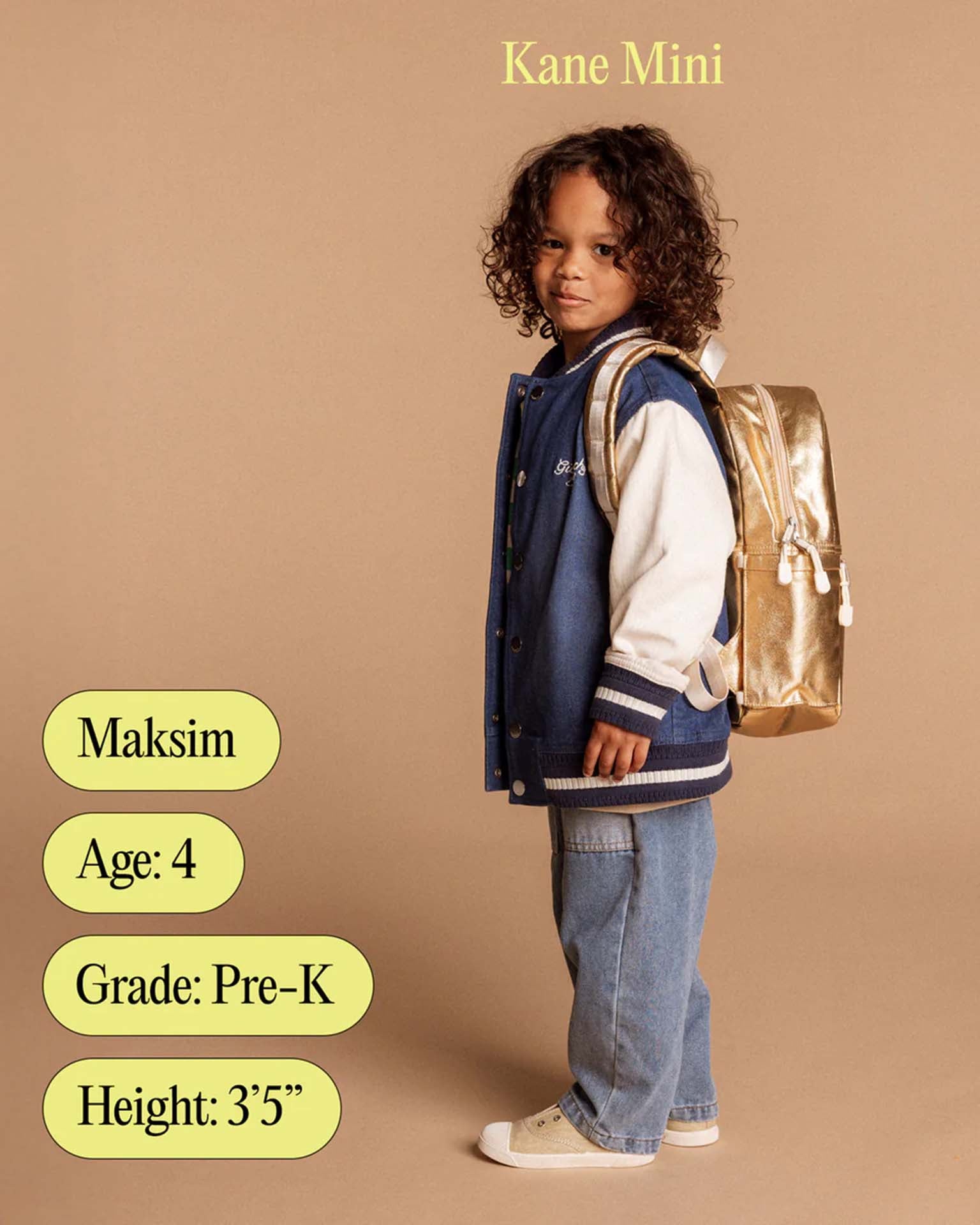 A young child with curly hair wears a blue jacket, jeans, and a State Bags Kane Mini Backpack in Navy, standing against a beige background. Text on the image reads: Maksim, Age 4, Grade Pre-K, Height: 35.