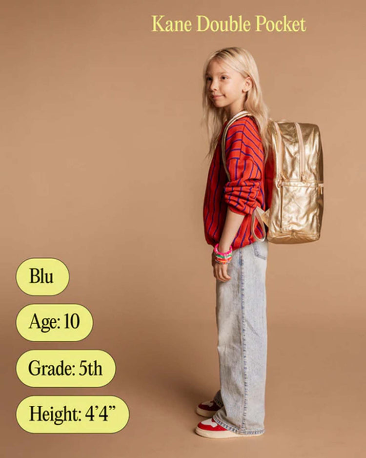 A young child with long blond hair wears a red striped shirt, blue jeans, and red sneakers, carrying a green Kane Double Pocket Backpack by STATE Bags, standing sideways against a beige background. Text displays name, age, grade, and height.