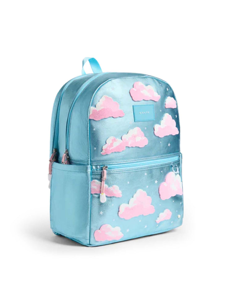 The Kane Double Pocket Backpack in Clouds from State Bags features a light blue design with pink clouds and small white stars, a front zip pocket, and a top blue handle—making it both a stylish and practical choice for school.