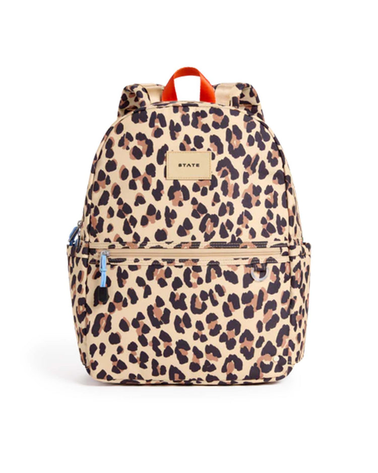 The STATE Bags Kane Backpack in Leopard features a beige background with a bold brown and black leopard print, a convenient front zipper pocket, handy side pockets, and a small rectangular STATE logo label on the front. Designed for school or travel, this backpack also includes an orange top handle for easy carrying.